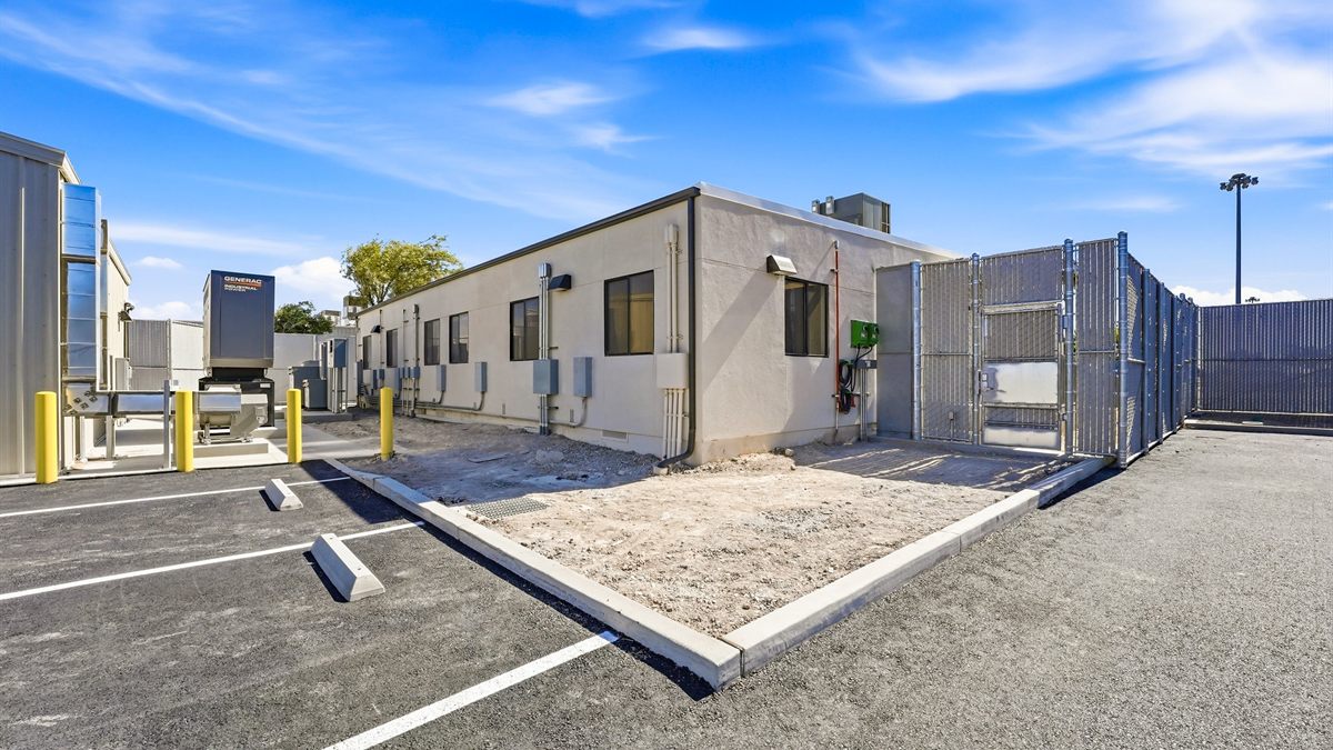 The completed building exterior with new asphalt paving, parking striping and concrete curbing, exterior electrical panels and conduit, a standby generator, and a secured gate.